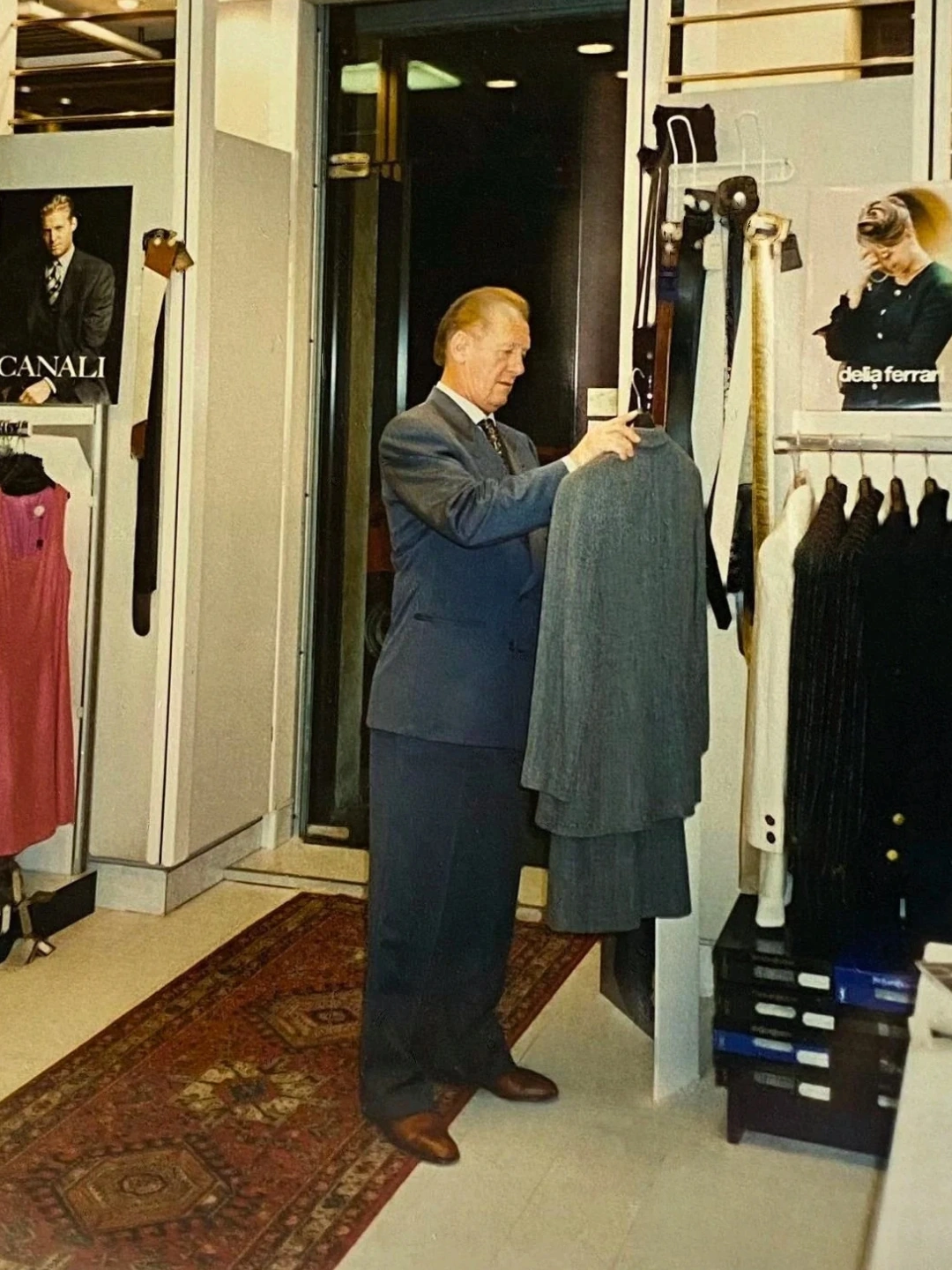 Rinaldo Danese, elegante in abito blu, sistema un capo esposto nel negozio